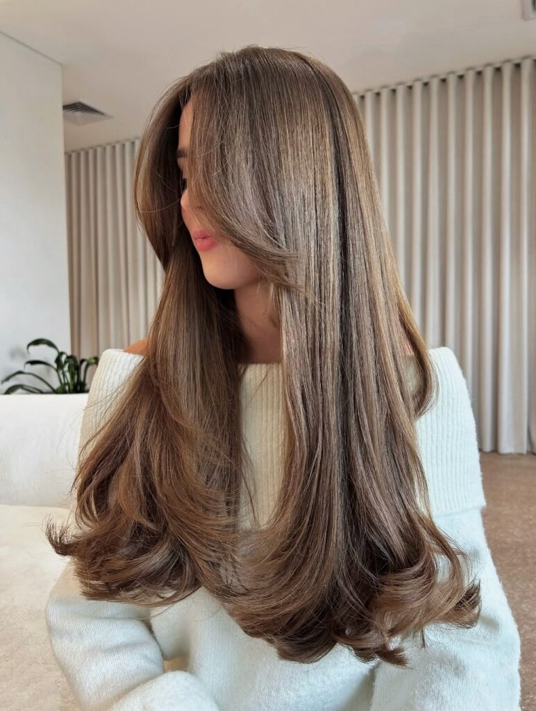 Long sleek caramel brown hair with balayage highlights and soft flipped-out layered ends.
