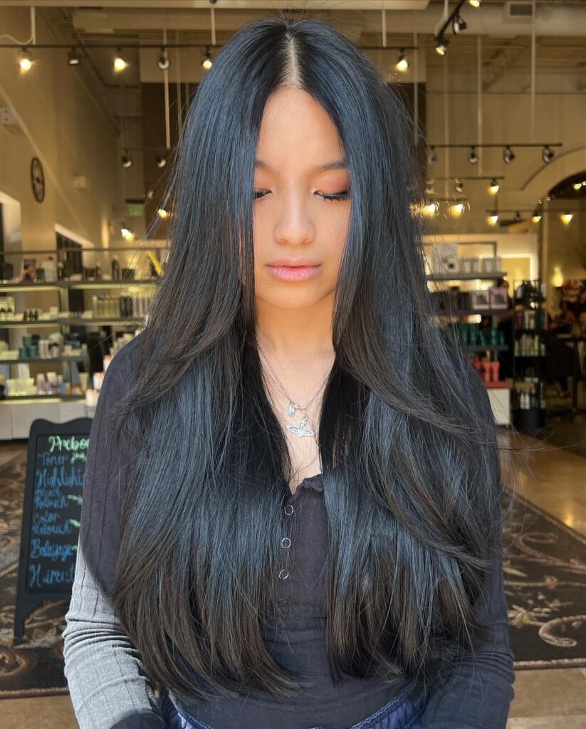 Long jet black hair with a middle part styled in soft, cascading waterfall layers.