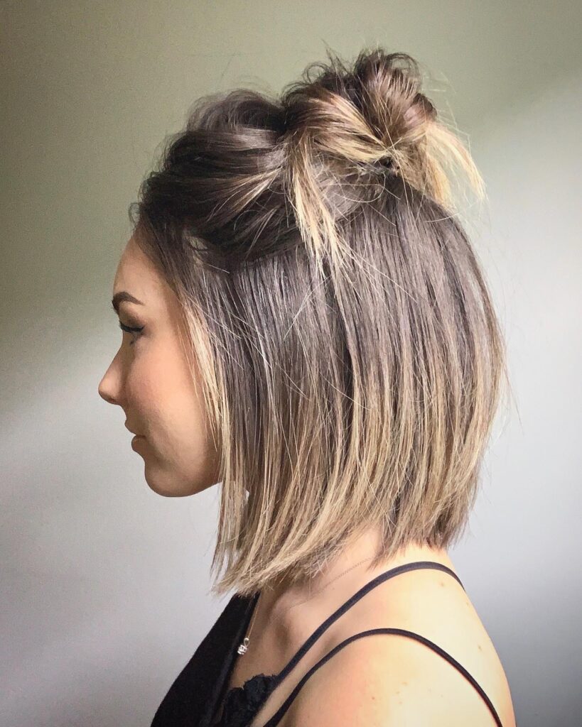 A woman with a sleek balayage angled bob styled with two small space buns on top.