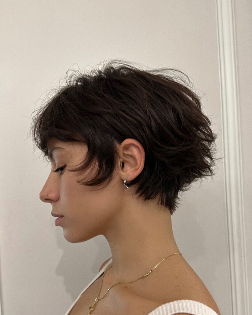 A woman with a shaggy brunette wolf cut pixie featuring feathered, layered texture.