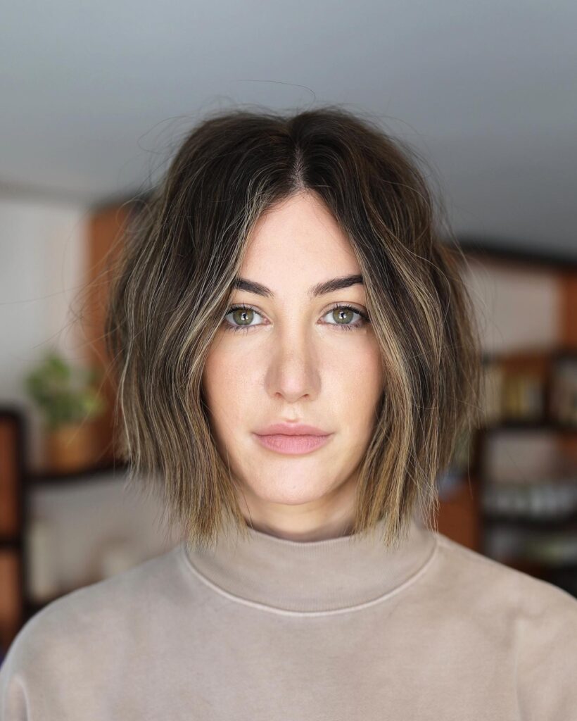 A woman with a wavy golden brown balayage bob styled with a center part.