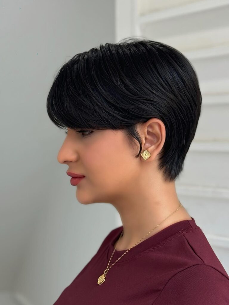 A woman with a sleek black side-swept pixie cut featuring a deep side fringe and glossy finish.