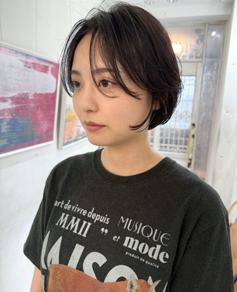 A woman with a black jaw length bob tucked behind one ear with soft wispy bangs.