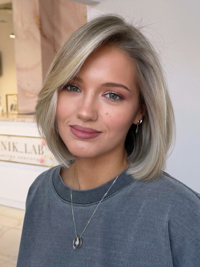 A woman with an ash blonde bob featuring a dramatic swoopy side bang.