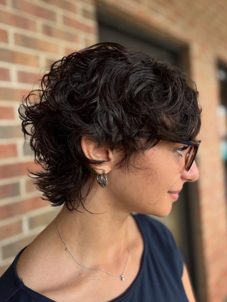 A woman with a dark brown curly shag haircut featuring layered, textured ends.
