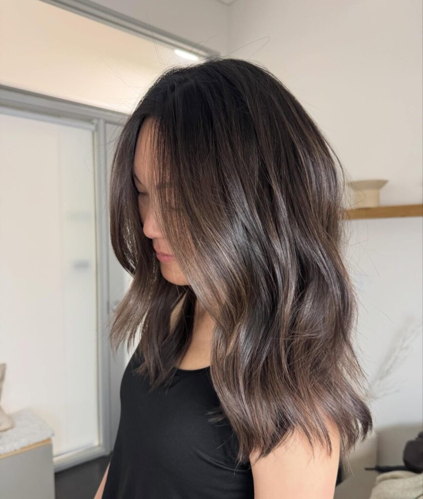 A woman with a dark brown layered shag haircut featuring face framing money piece highlights.