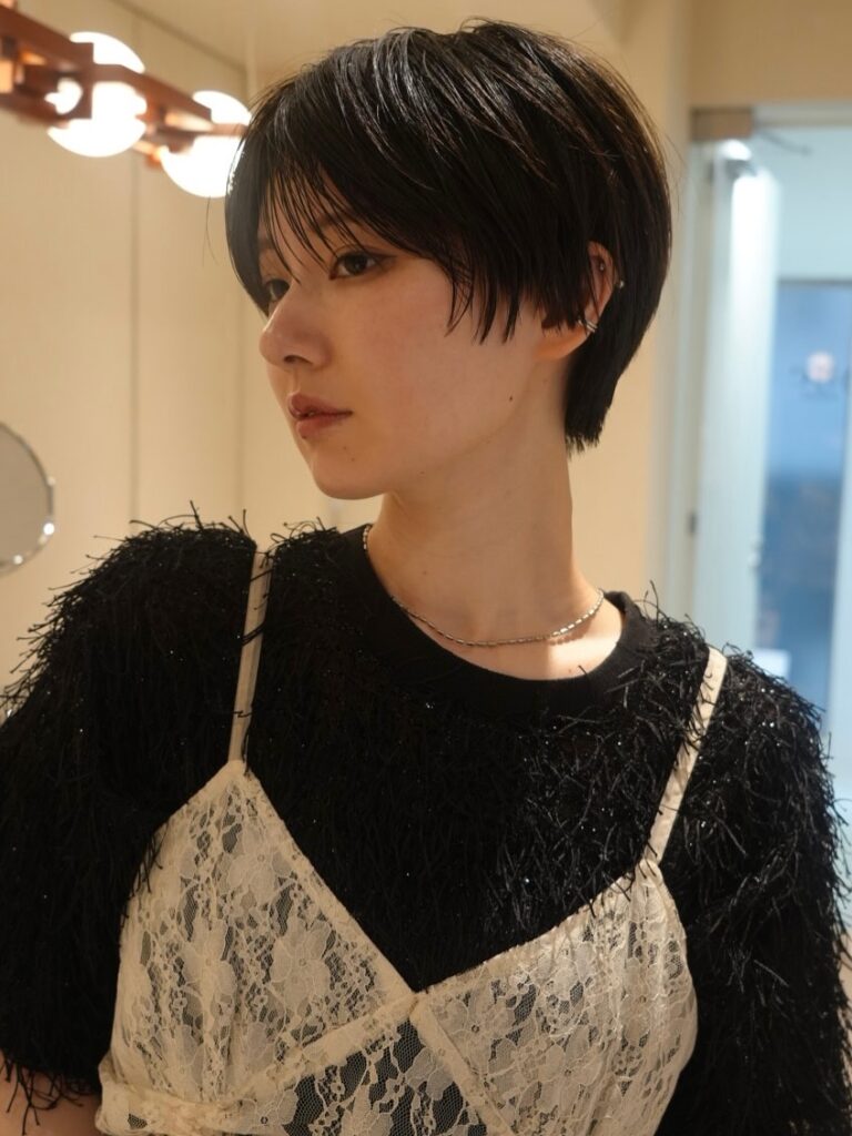 A woman with a sleek black side swept pixie cut and soft side bangs poses in a black and white outfit.