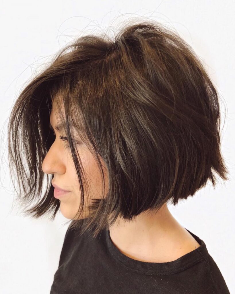 A woman with a chin-length choppy brunette bob featuring face-framing layers and subtle caramel highlights.