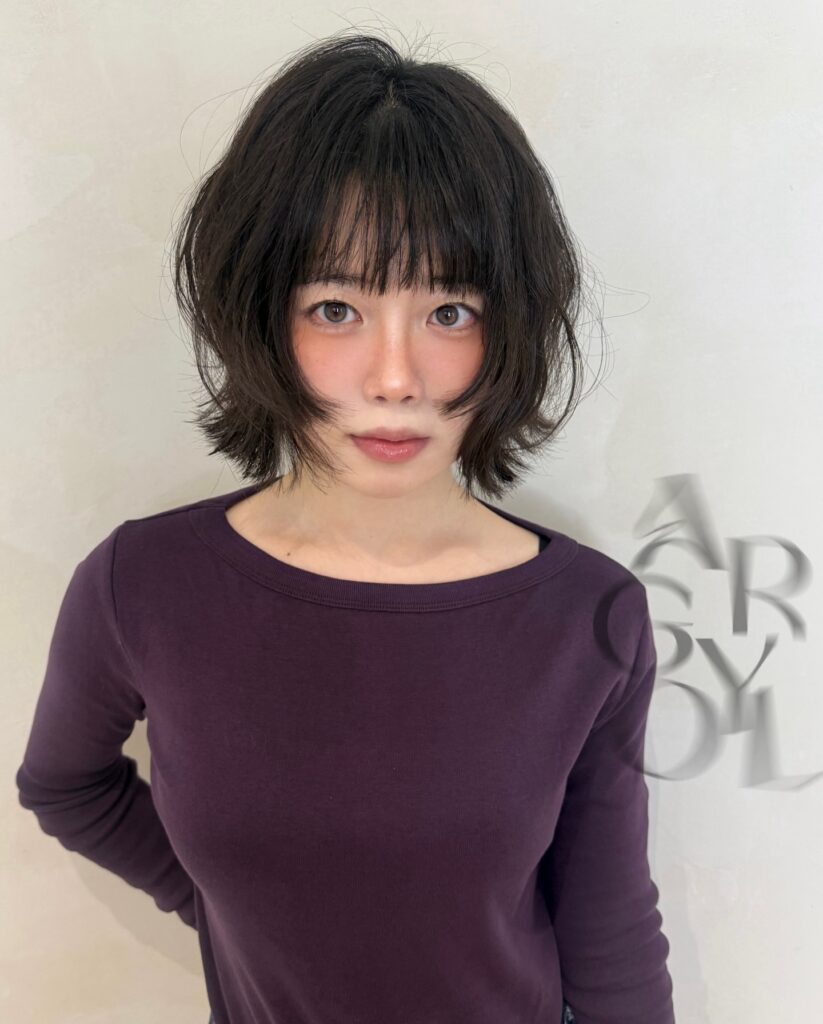 A woman with a fluffy black wolf bob and full wispy fringe.