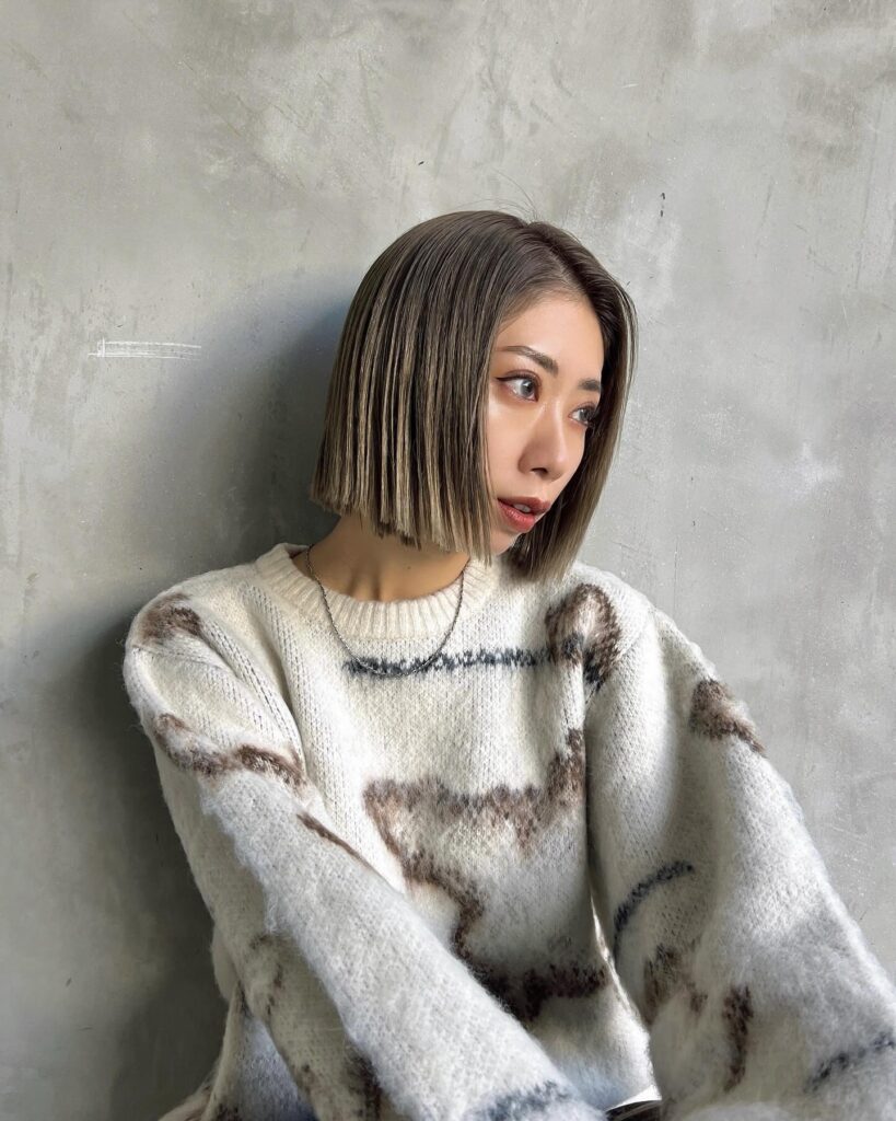 A woman with a sleek blunt chin length bob featuring caramel and ash highlights.