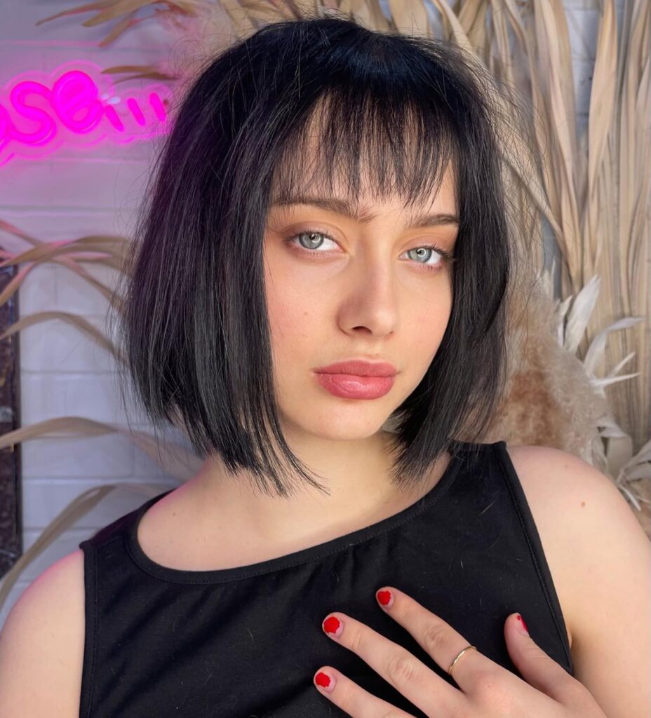 A woman with a jet black chin length piecey bob and full blunt fringe.
