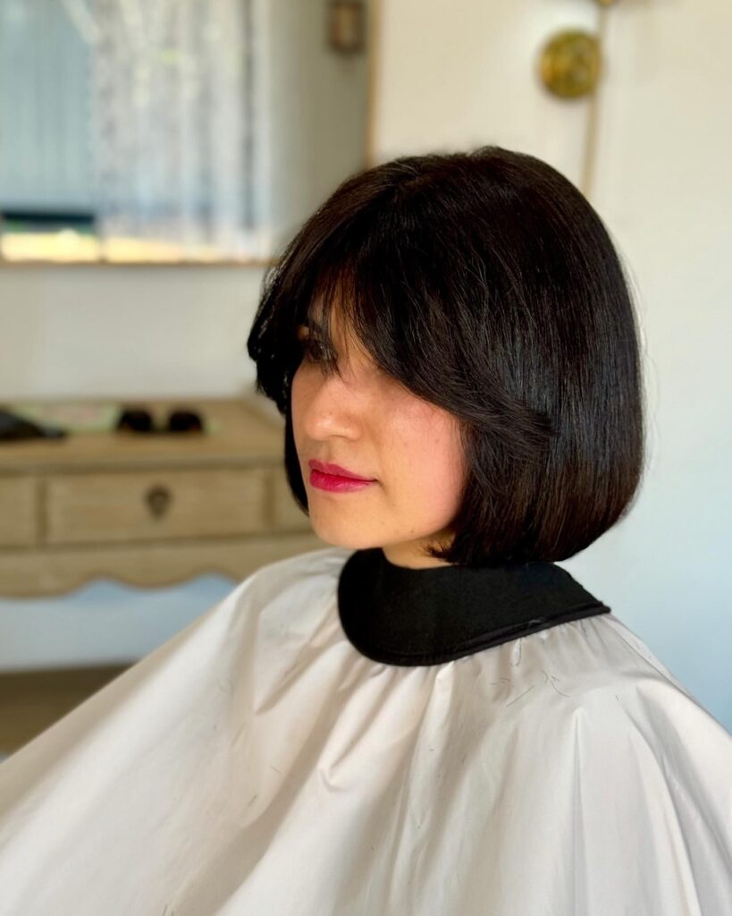 A woman with a jet black rounded bob and wispy curtain fringe.