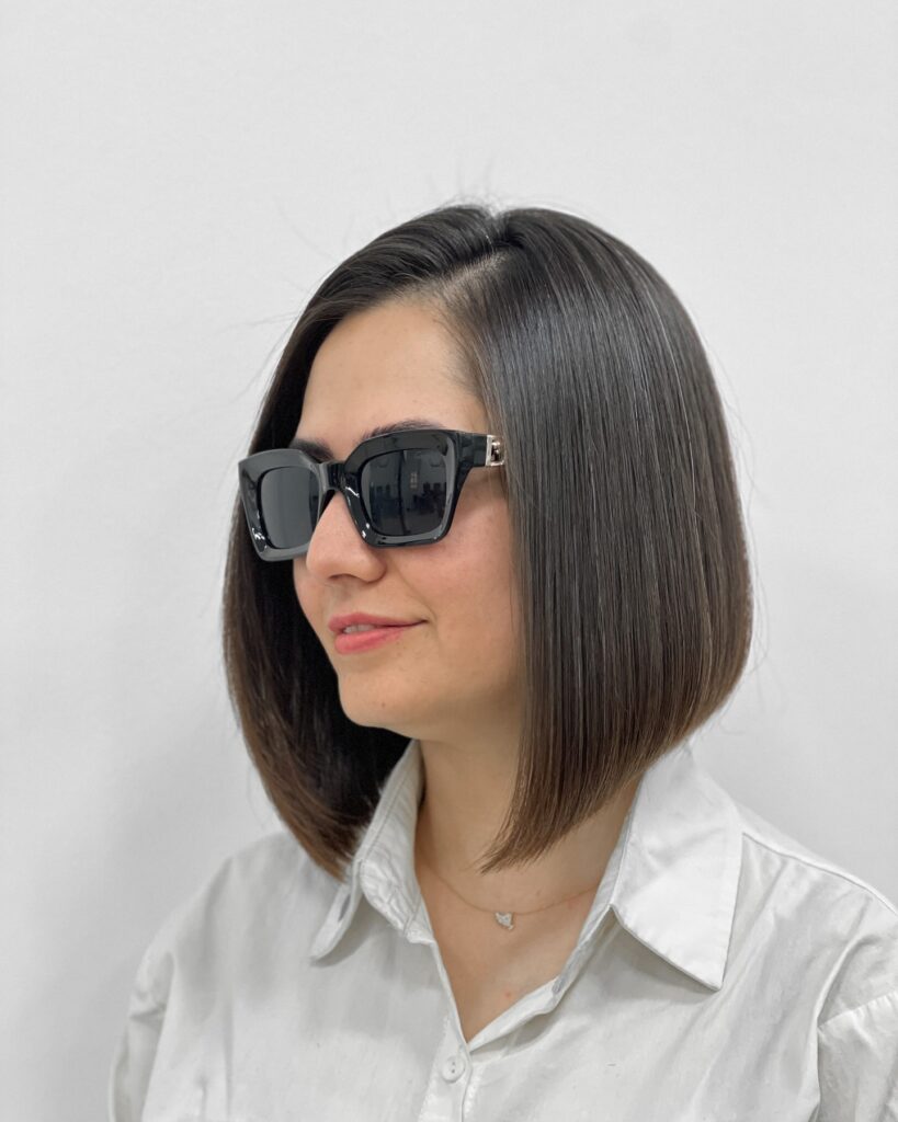 A woman with a glossy shoulder length brunette bob with a deep center part.