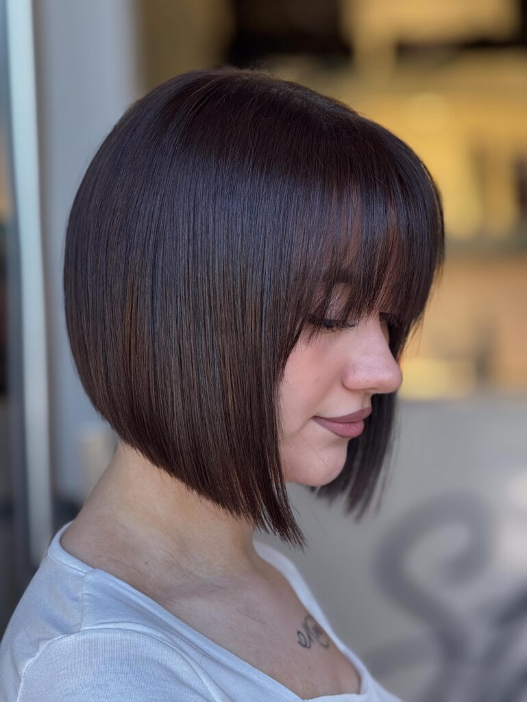 A woman with a sleek graduated chocolate brown bob and full blunt bangs.