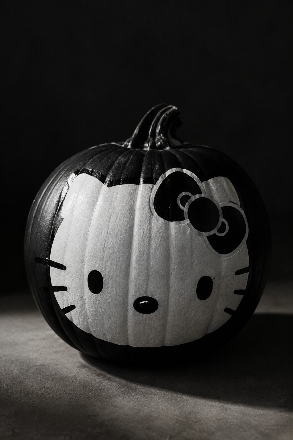 A black and white painted pumpkin with a Hello Kitty face, bow, and whiskers on a dark surface.
