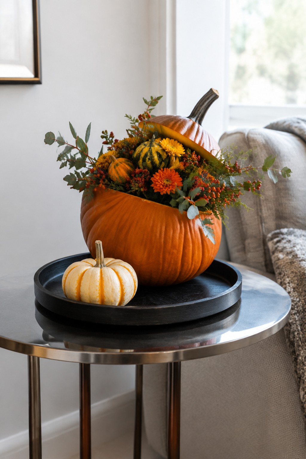 A large orange pumpkin with its top cut off sits on a black tray and holds a mix of flowers, berries, and smaller pumpkins.