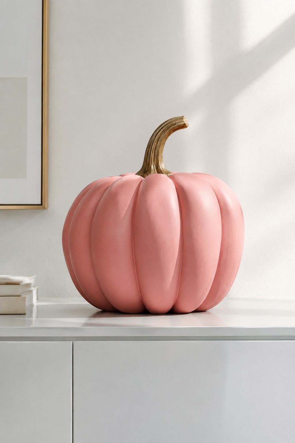 A large matte pink pumpkin with a gold stem sits centered on a white console table against a plain wall.