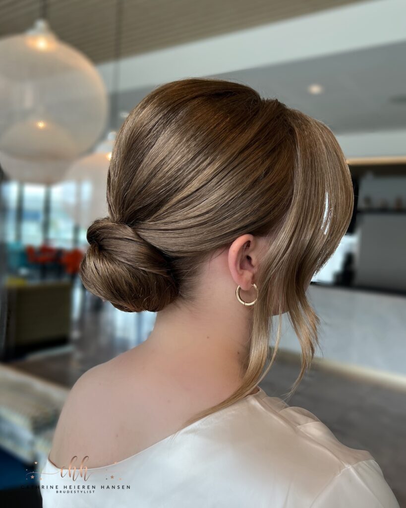A woman with light brown hair styled in a sleek low bun with a deep side part.