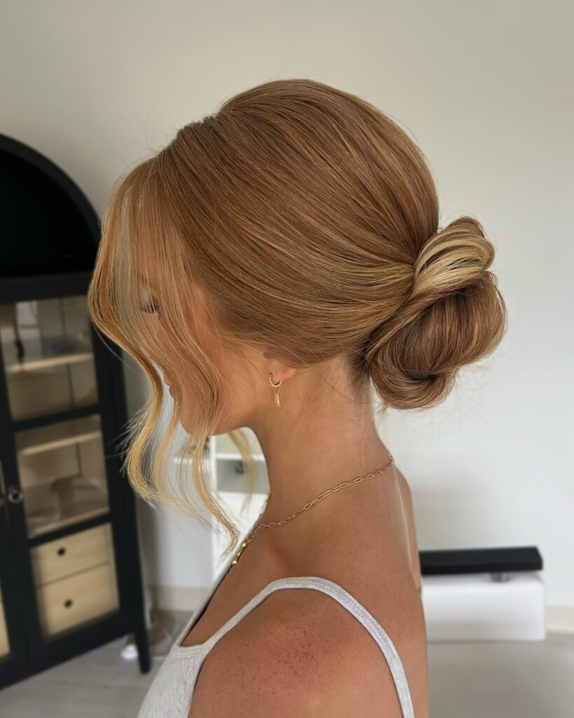 A woman with honey blonde hair styled in a smooth low bun with soft face-framing strands.