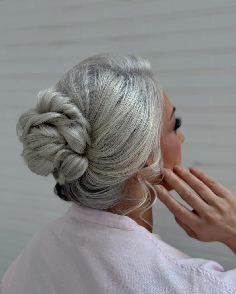 A woman with icy platinum silver hair wears a sleek twisted bun positioned low behind the ear.