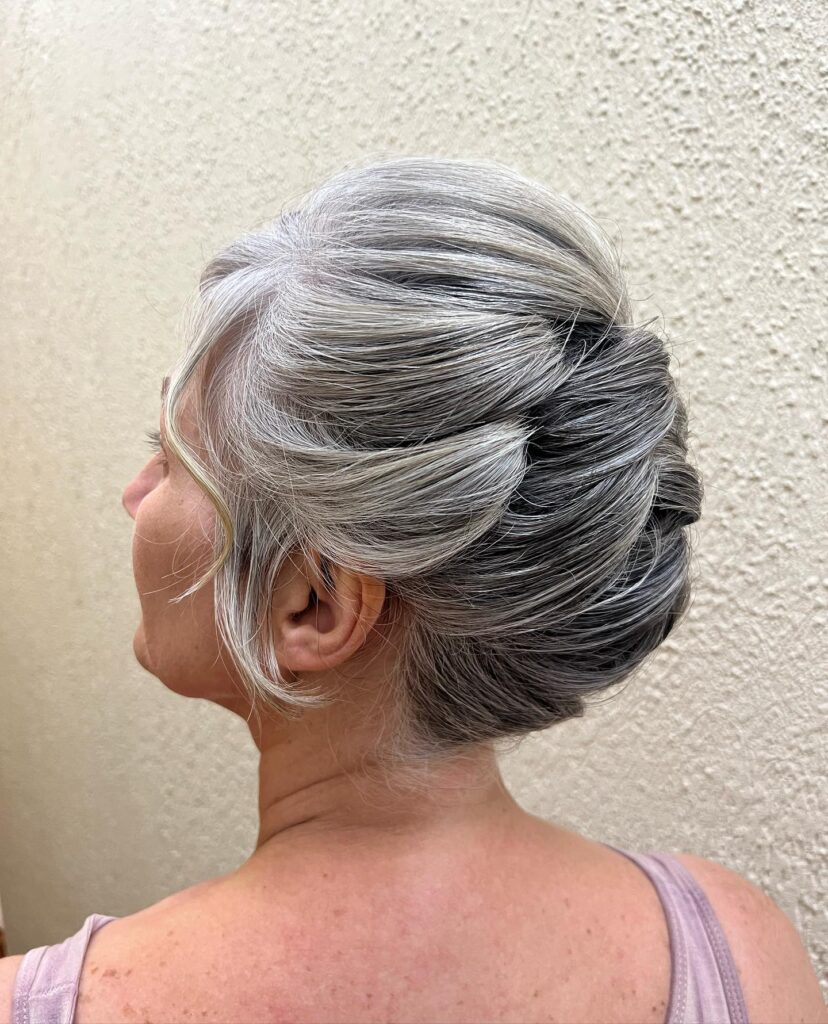 A woman with salt and pepper gray hair wears a sleek sculpted French twist updo.