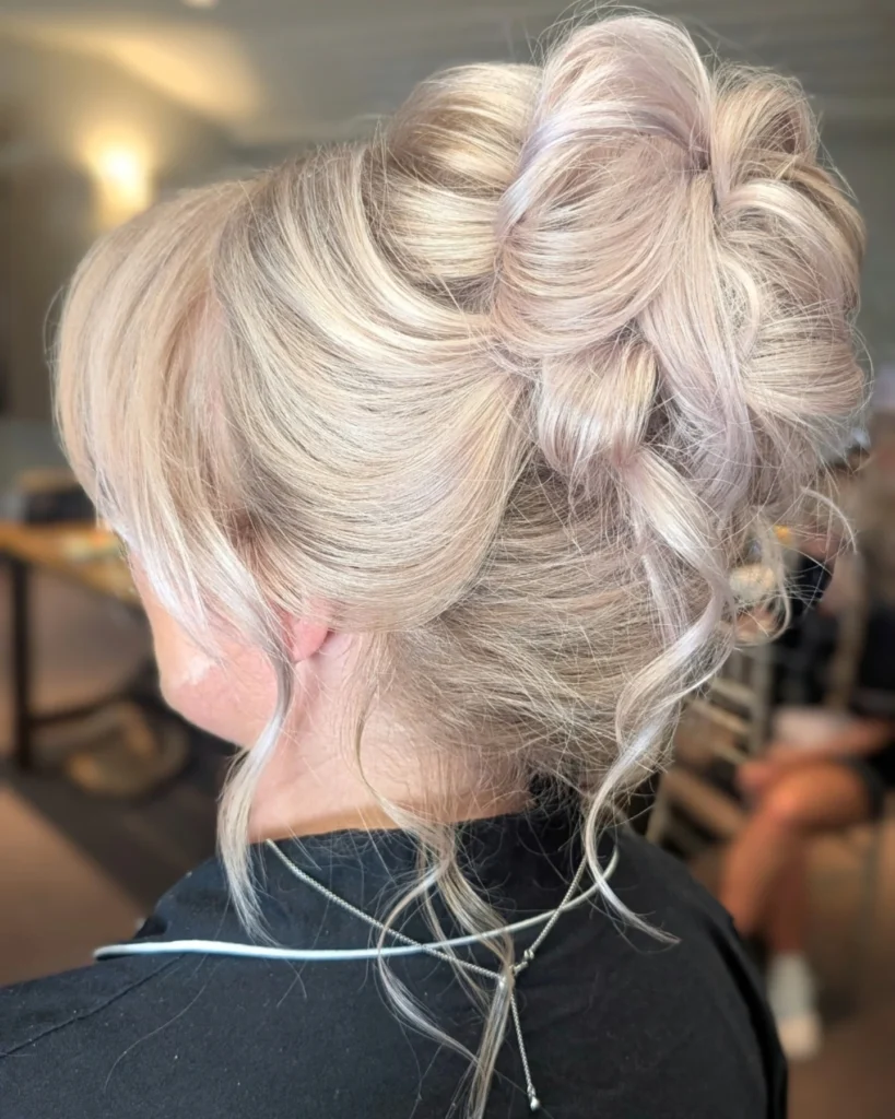 A woman with pale platinum blonde hair wears a voluminous curly bun with loose face-framing tendrils.