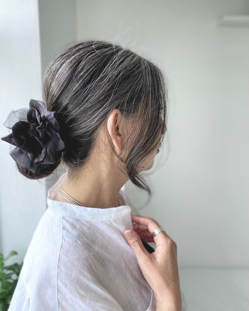 A woman with salt and pepper hair wears a sleek low bun accented with a large black fabric flower.
