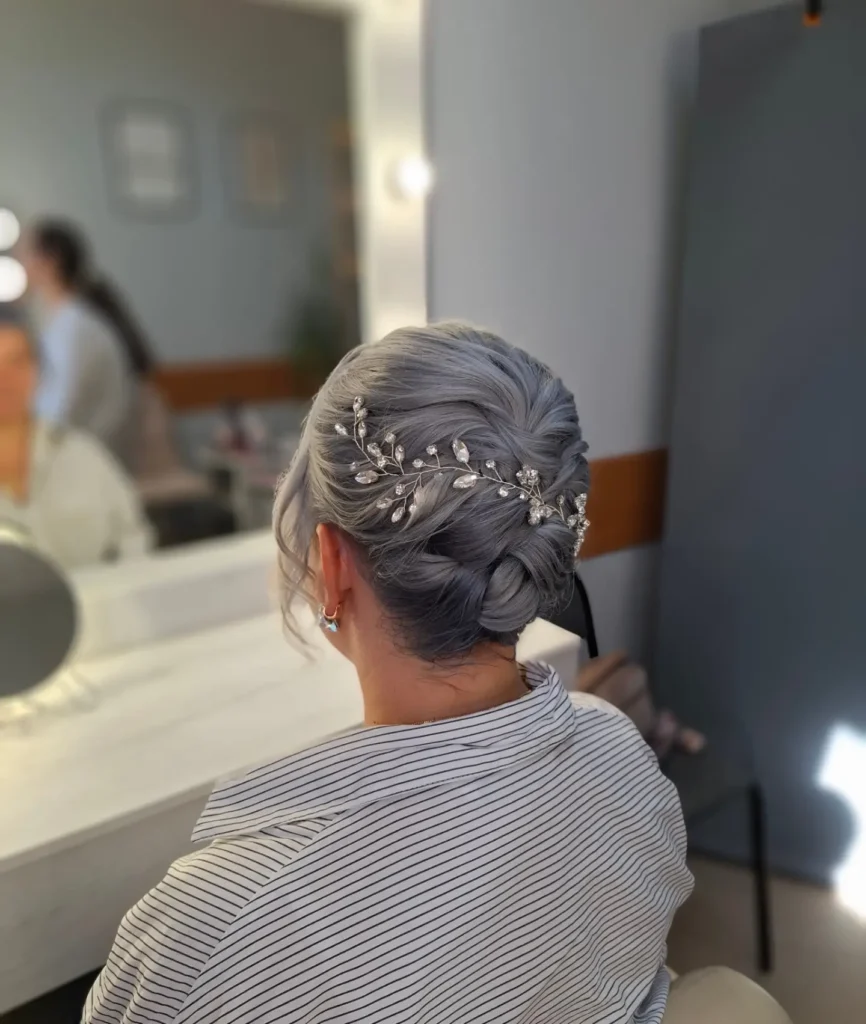 A woman with steel gray hair wears a braided updo accented with a sparkly crystal hair vine.