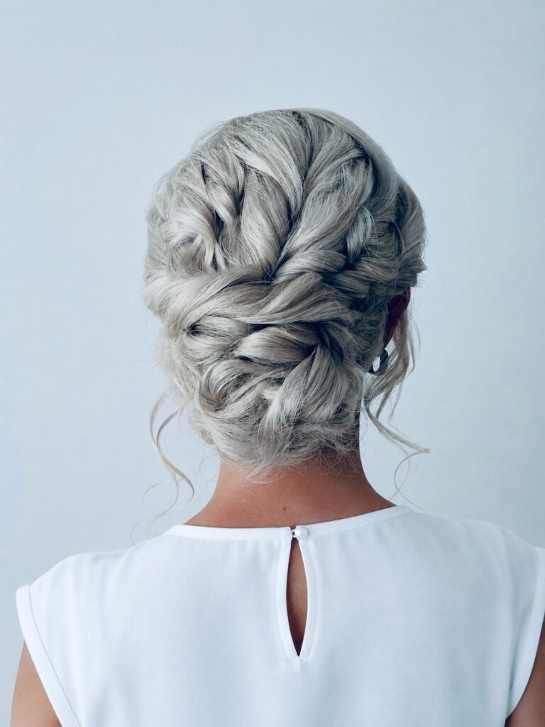 A woman with platinum silver hair wears a textured rope braided updo with soft face-framing tendrils.
