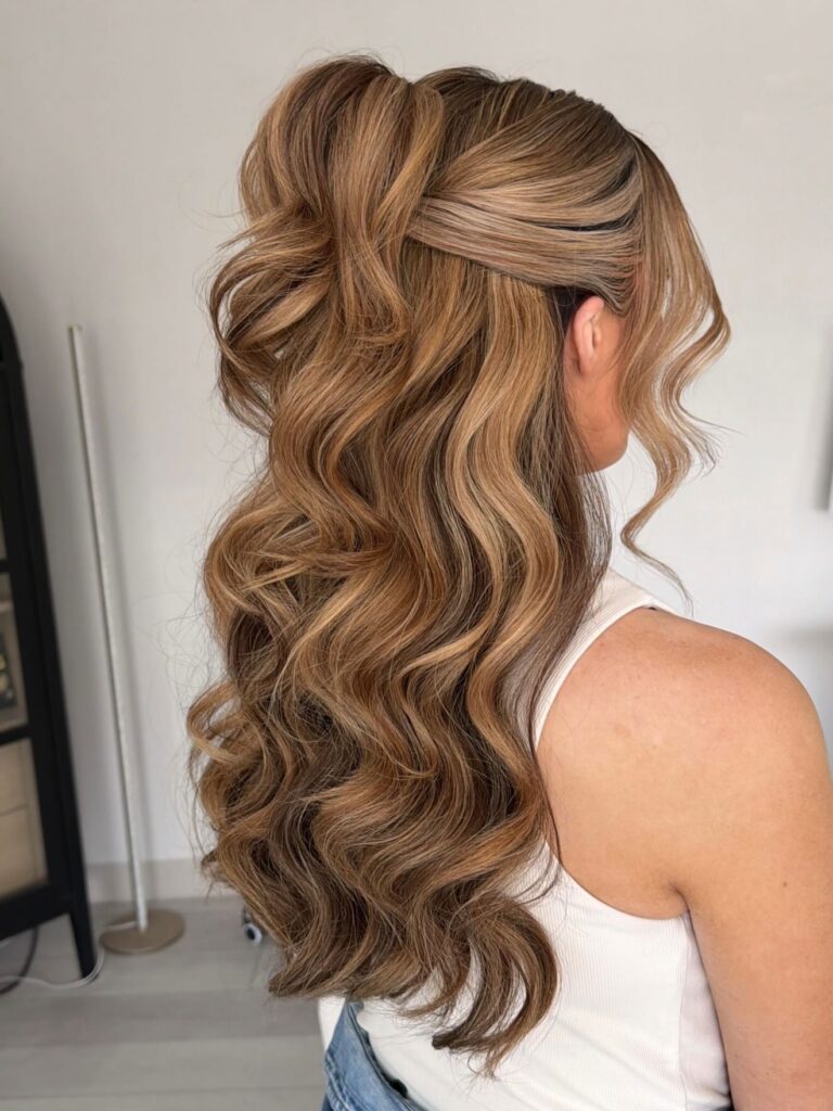Long honey blonde hair styled in a high half ponytail with bouncy curls cascading down the back.