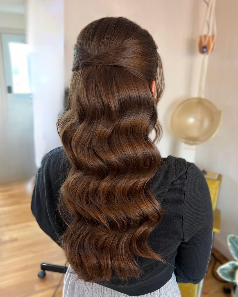 Long chocolate brown hair styled in glossy Hollywood waves with a smooth twisted half up detail at the back.