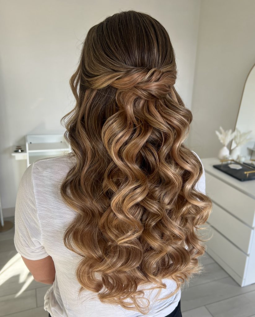 Long honey blonde hair styled in a half up twisted design with defined curls flowing down the back.