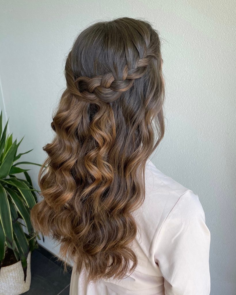 A woman with long dark and light brown hair in a horizontal crown braid with waves falling down.