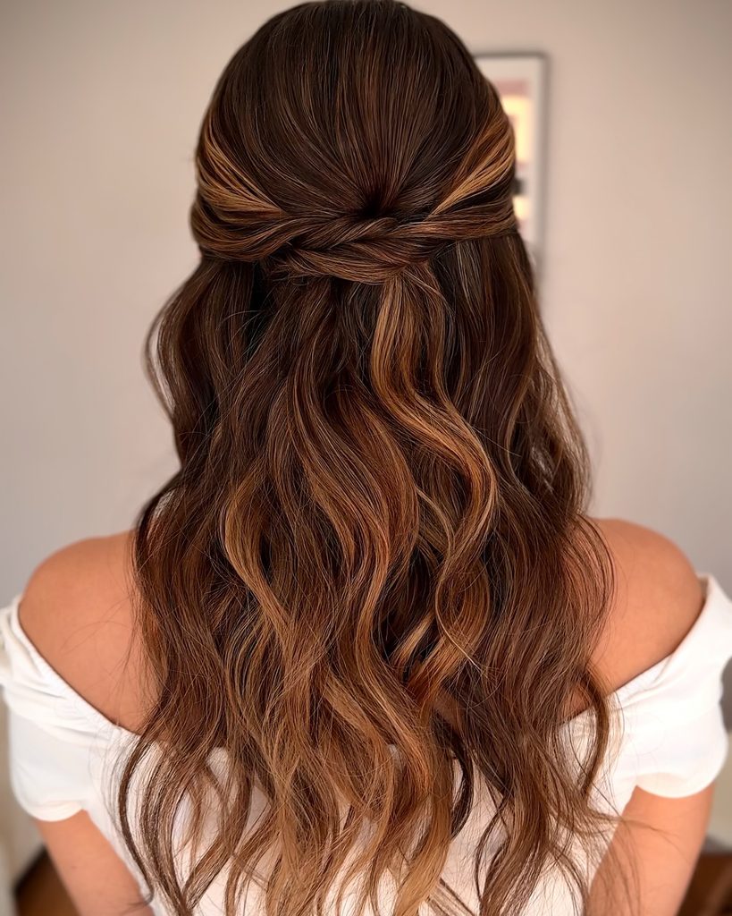 Medium length brunette hair styled in a half up crossover twist with caramel highlights and soft loose waves.