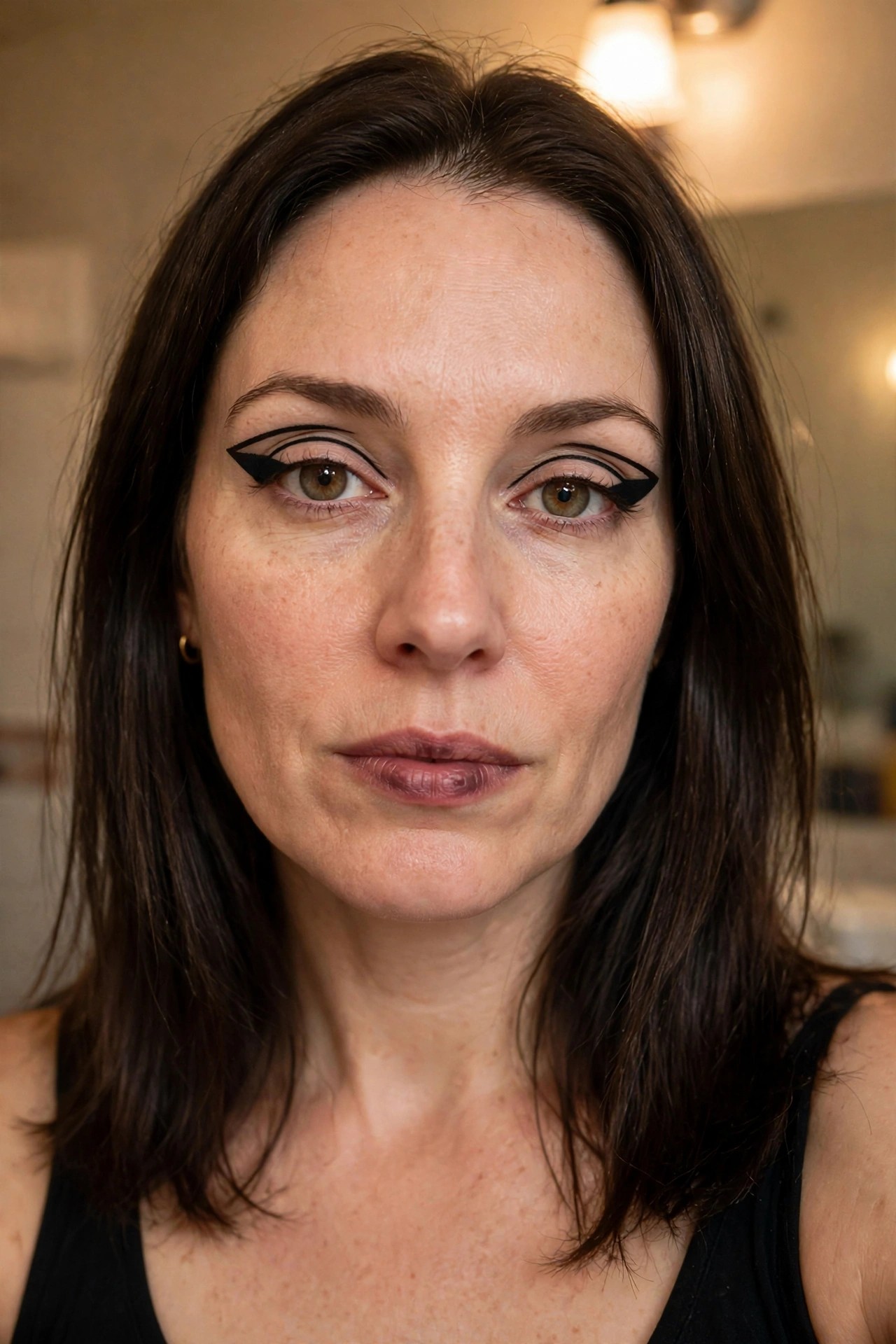 Close-up of a woman wearing bold black graphic eyeliner with thick extended wings on both eyes and neutral matte lips.