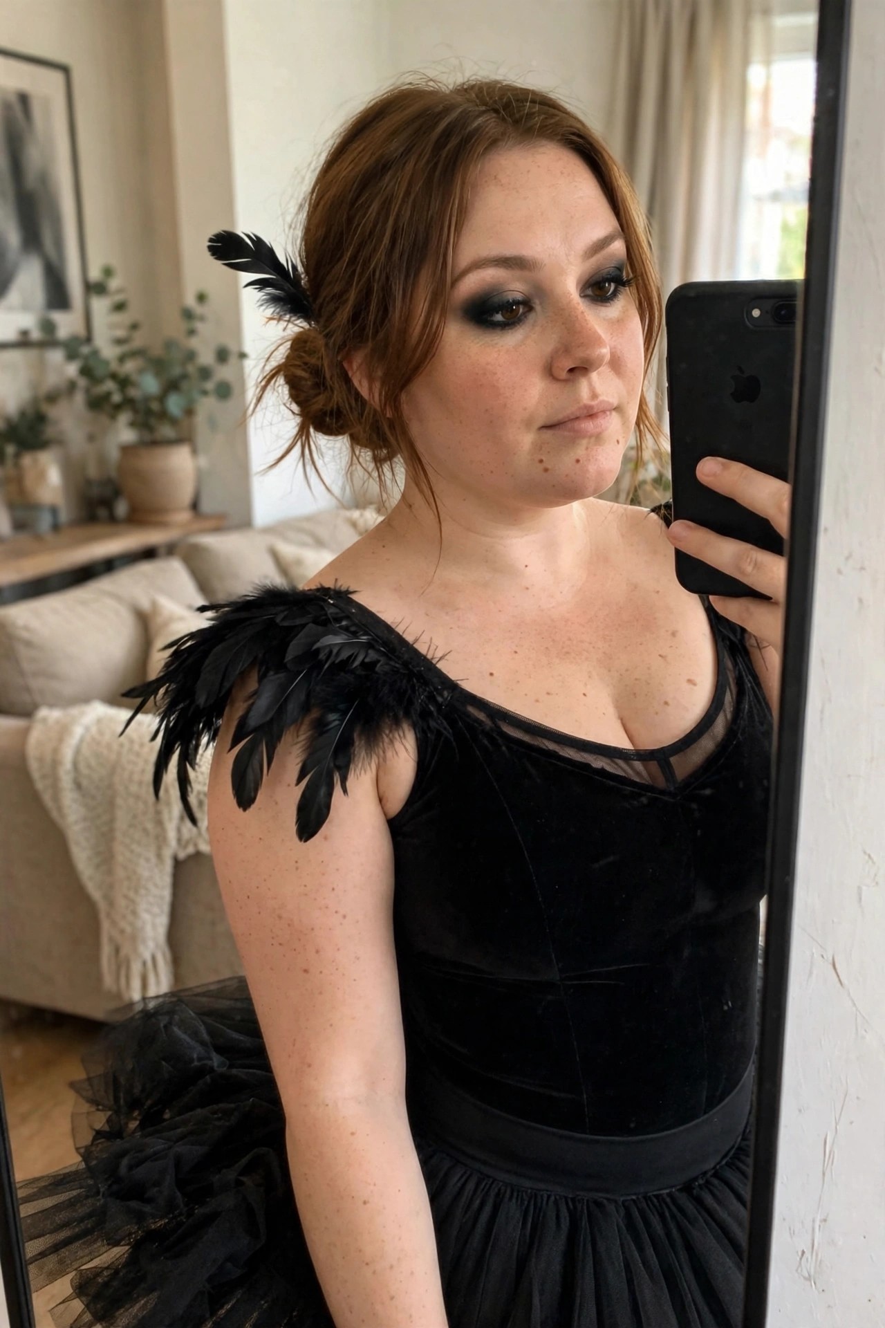 Woman with brown hair in a bun wearing a black velvet dress with feather shoulder accents and a black tulle skirt for a black swan costume.