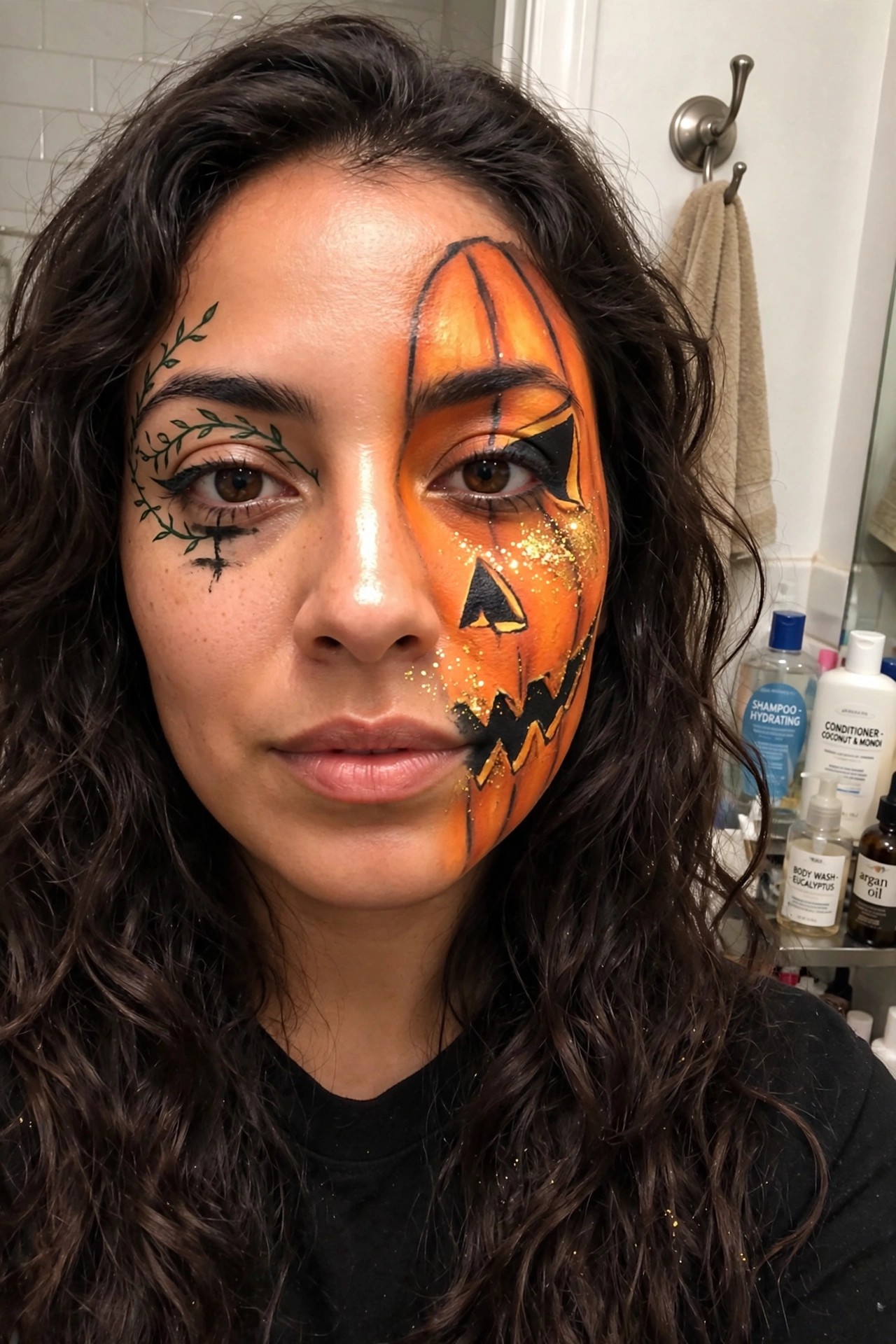 Close-up of half-face pumpkin makeup with orange base, black jack-o'-lantern features, gold glitter, and green vine details around the opposite eye.