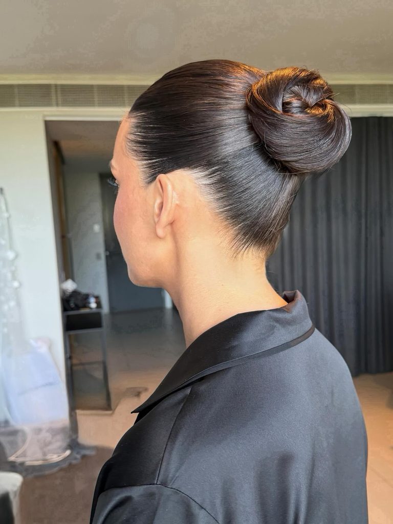 Side view of a woman with glossy dark brown hair in a sleek slicked-back high bun with a swirled top.