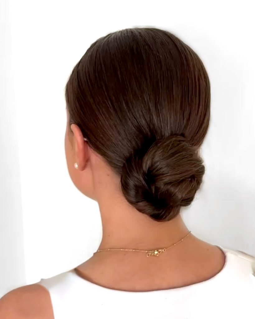 Back view of a woman with glossy chestnut brown hair in a smooth slicked-back low twisted bun.