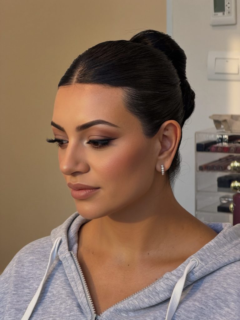 Side view of a woman with dark espresso hair in a glossy center-parted slicked-back high bun.