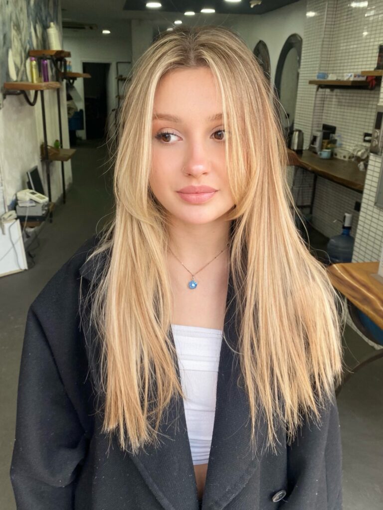 A woman with long honey blonde hair featuring sun kissed highlights and feathered layers with a middle part.