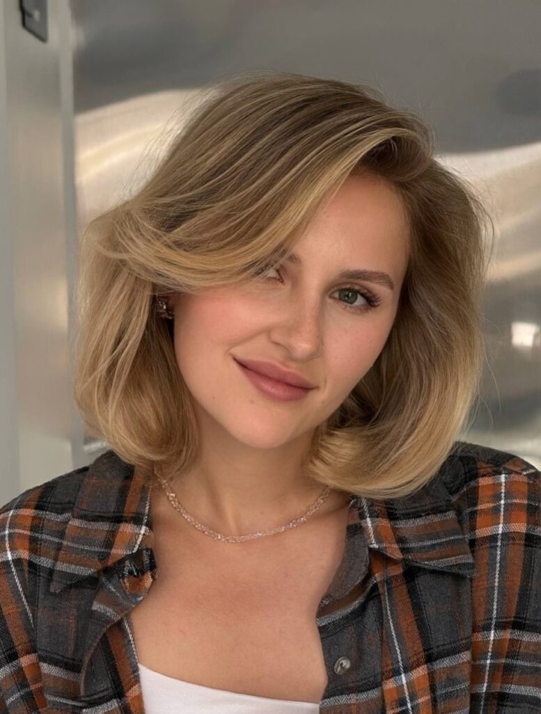A woman with a chin length dirty blonde bob styled with a dramatic curled flip and deep side part.