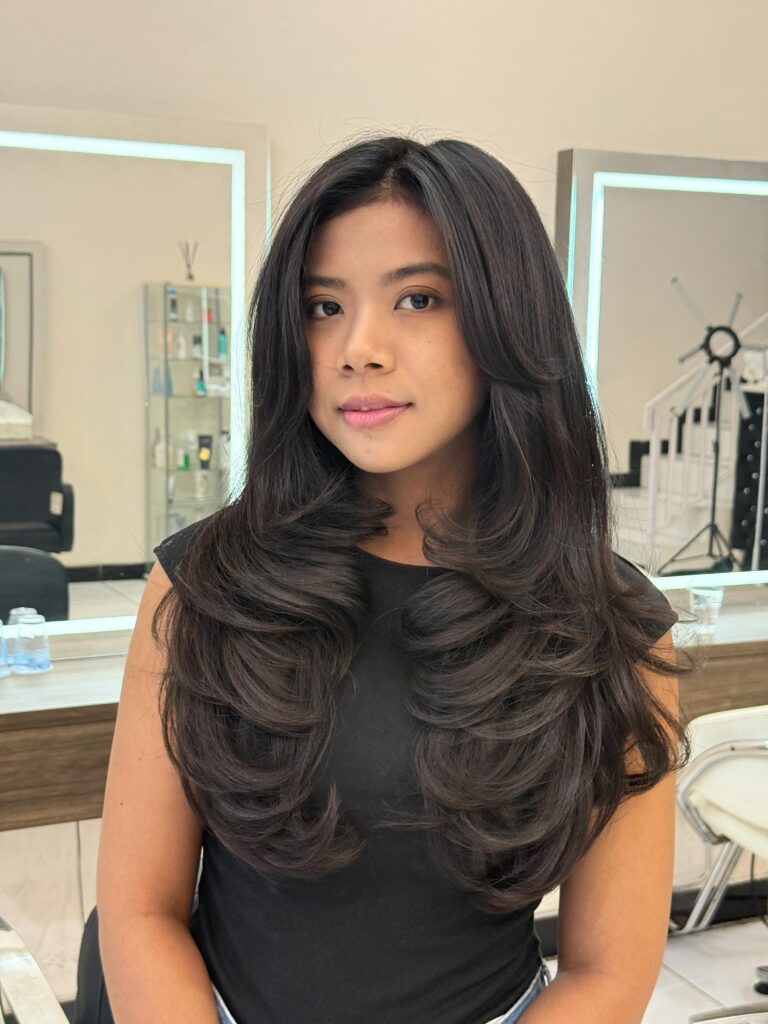 A woman with extra long dark brown hair styled in heavy flipped butterfly layers with a middle part.