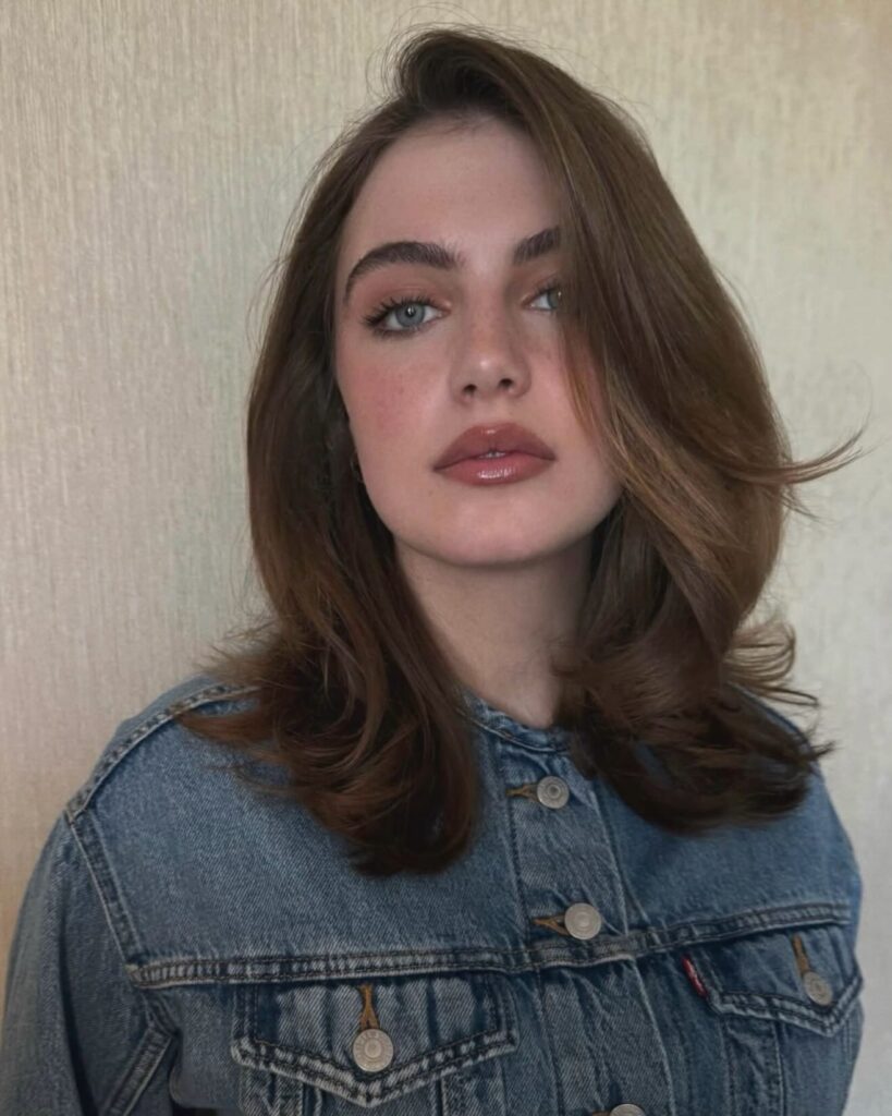 A woman with medium length brown hair styled with swept back volume on top and softly flipped layers.