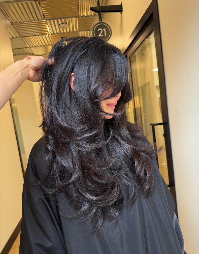  A woman with long black hair featuring glossy, voluminous layers curled outward at the ends.