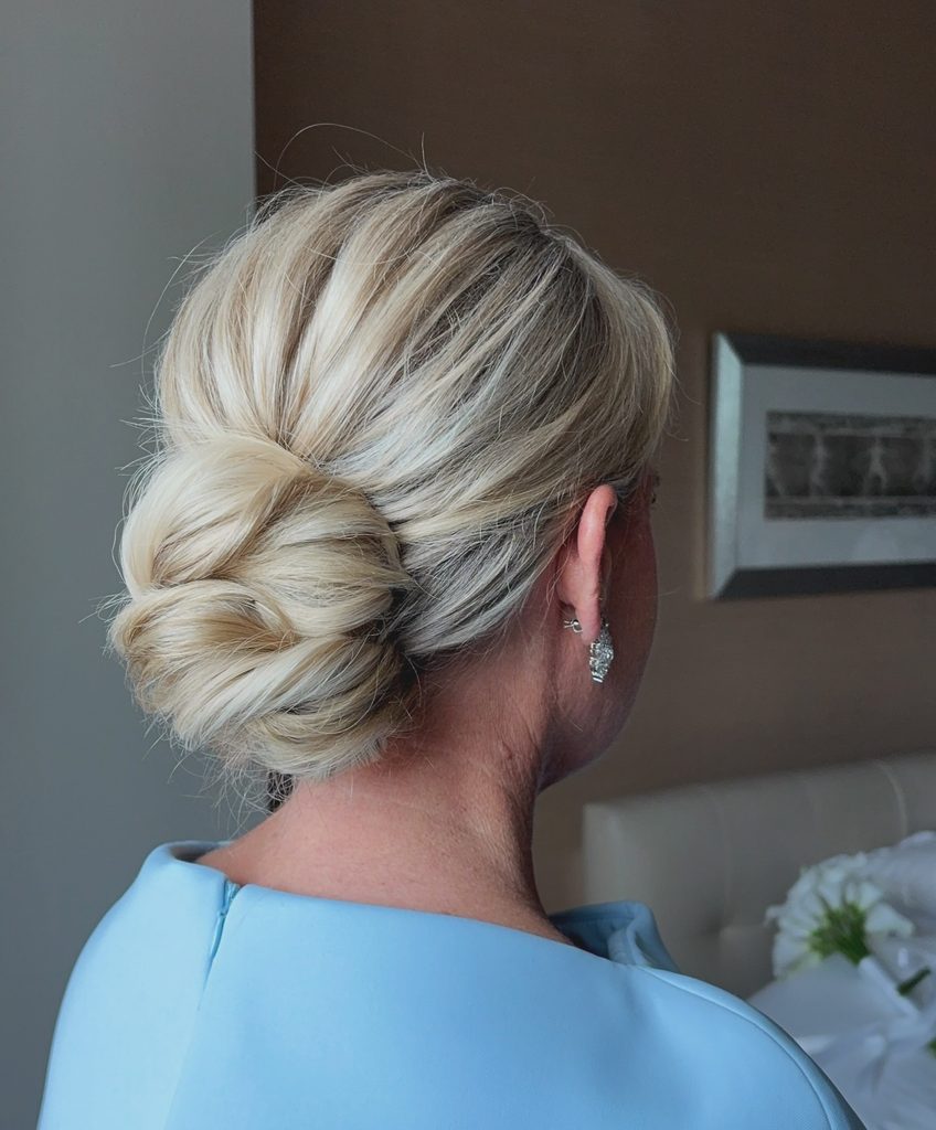 Back view of a woman with platinum blonde hair styled in a polished low chignon with a smooth swept-back crown and sparkly drop earrings.