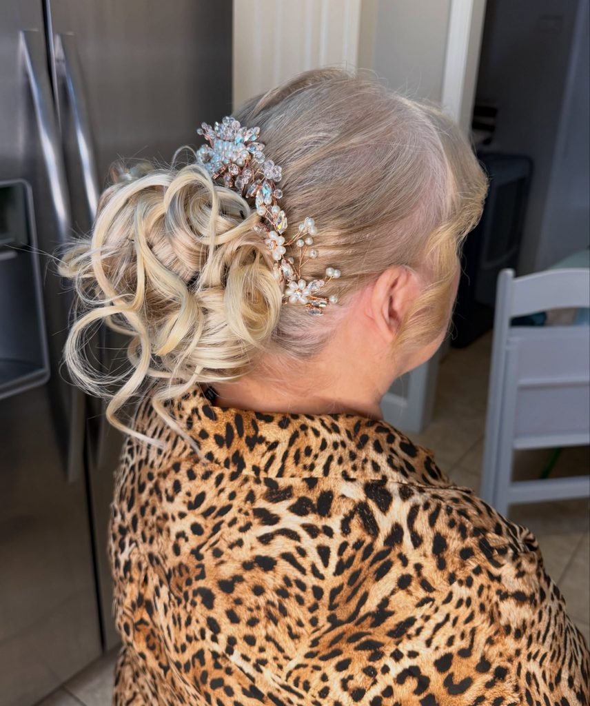 Side view of a woman with champagne blonde hair styled in a curly updo with a smooth crown and a pearl and crystal hair comb.