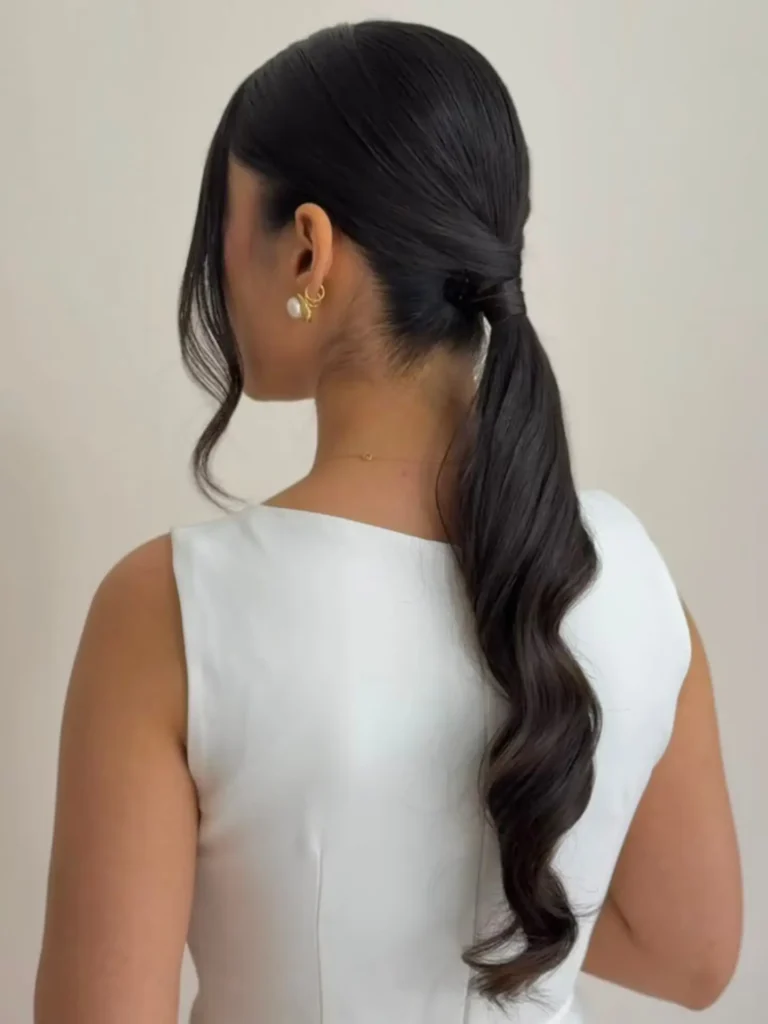 A woman seen from the back wearing a sleek black low ponytail with glamorous waves and face-framing strands.