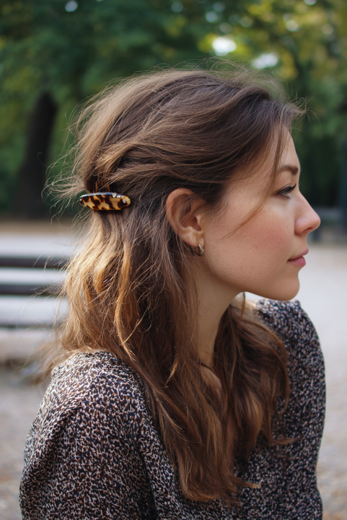 A woman with wavy brunette hair wears a simple half up style secured with a small tortoiseshell barrette at the side.