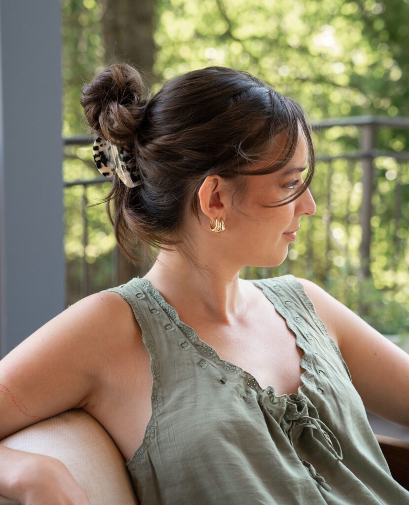 A woman with dark brunette hair wears a loose, textured top knot secured with a tortoiseshell claw clip and soft face framing pieces.
